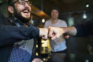 Man in a bar, fist bumping his friend, enjoying drinks together
