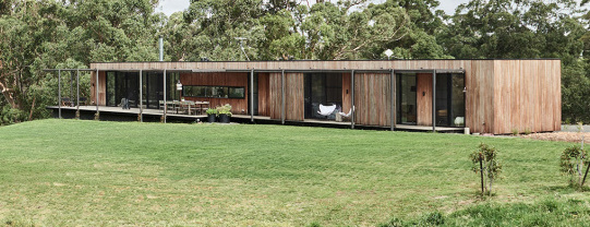 Image of prefabricated home with timber linings, opening onto a deck and lawn area